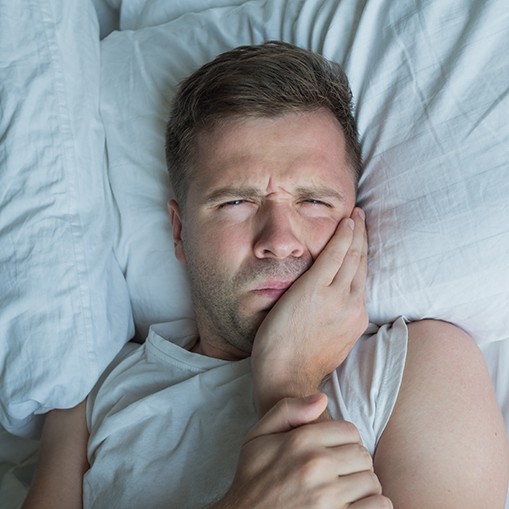 Man lying in bed rubbing his tooth in pain