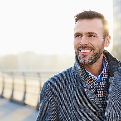 Man in grey coat walking across a bridge in the city