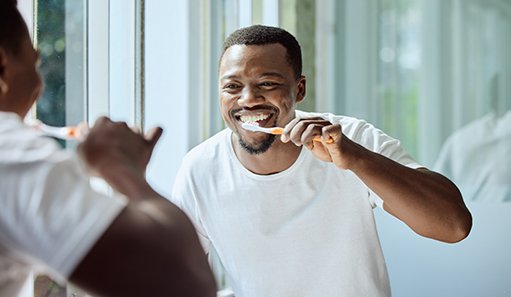 Man in white shirt looking in mirror brushing his teeth