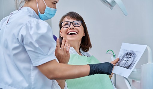Woman smiling with dentist while reviewing X-ray
