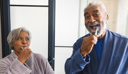 Couple smiling while brushing teeth in bathroom