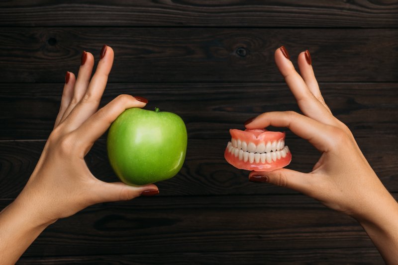 A green apple and dentures held by a doctor